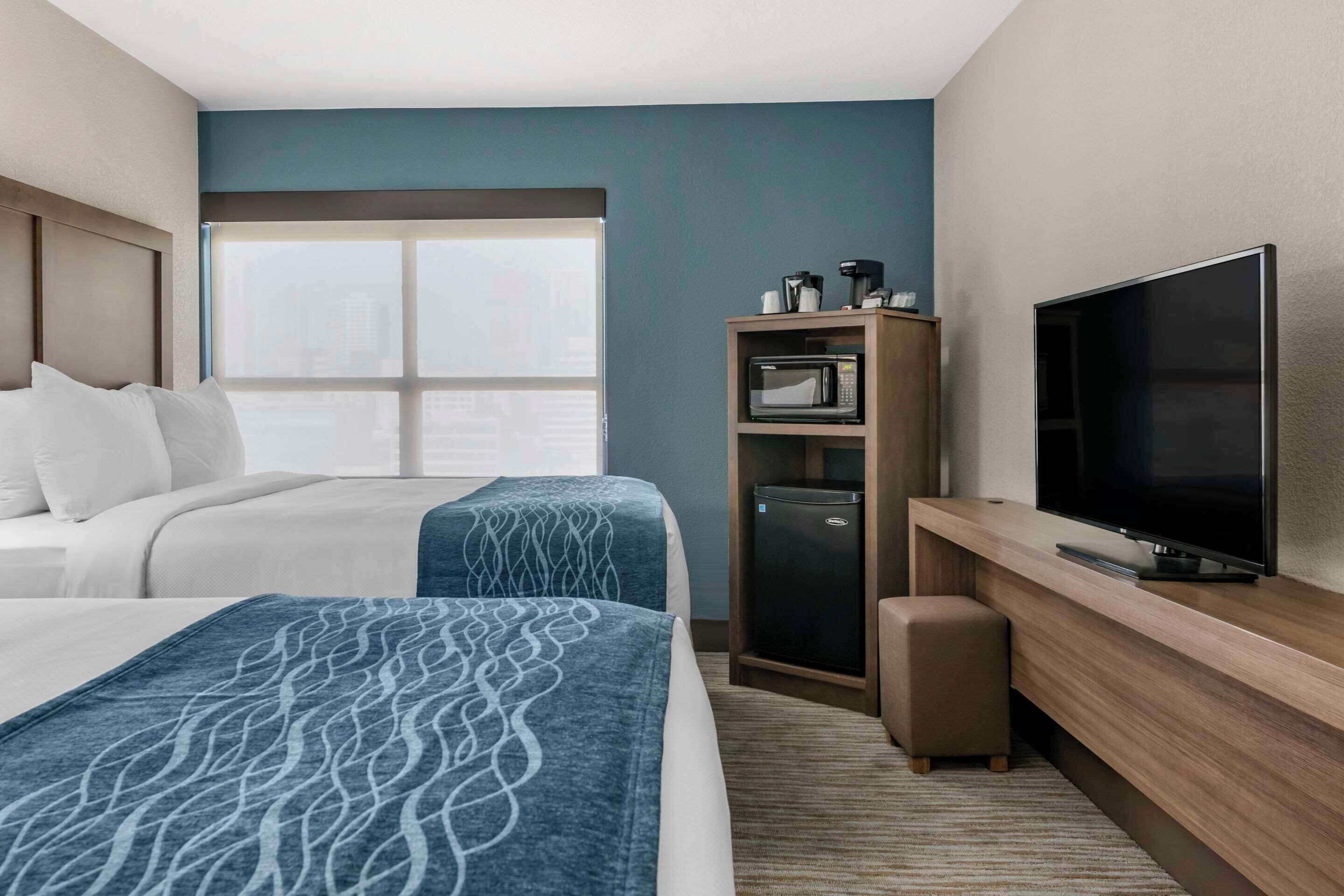 A hotel room with two beds, a television, a minibar, and a large window.