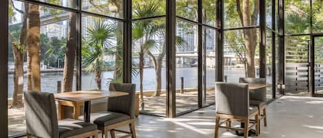 A modern indoor seating area with large windows overlooking a body of water and palm trees.