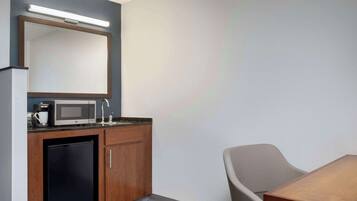 A compact hotel room with a kitchenette, a microwave, a coffee maker, a sink, and a chair.