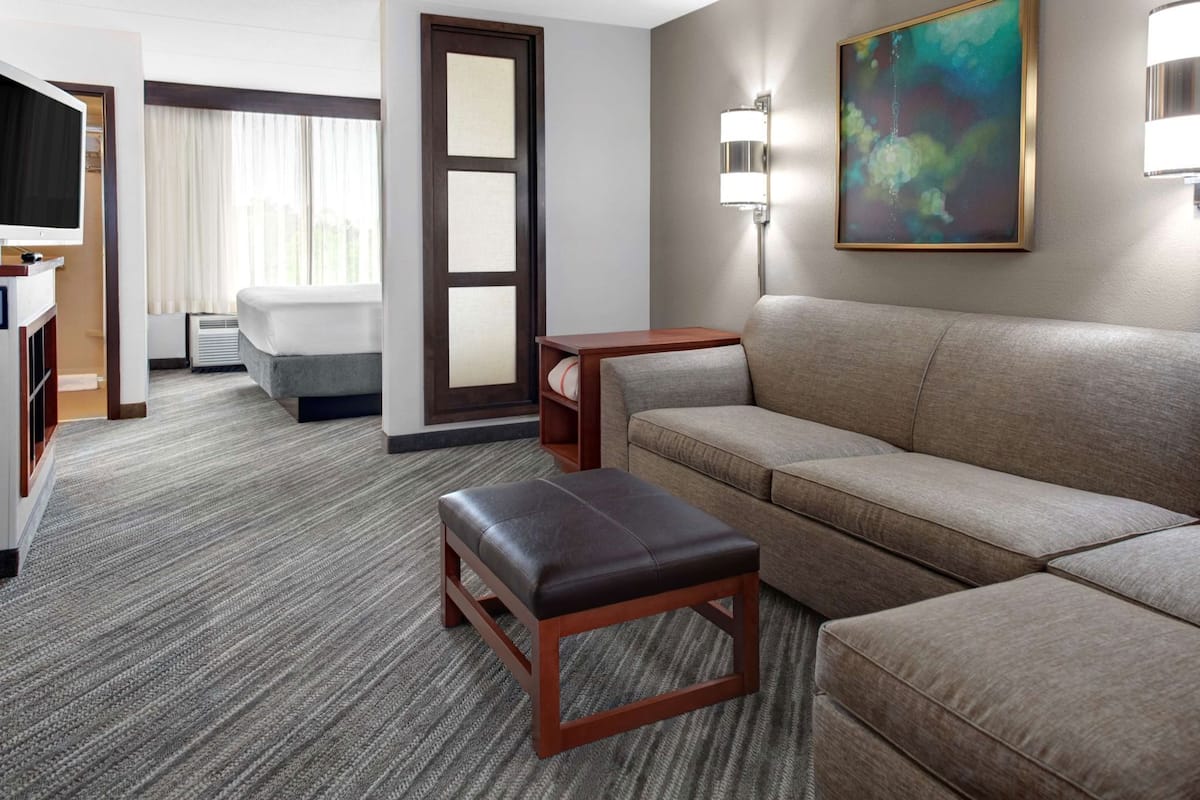 A hotel room with a sofa, a small table, a TV, a painting, and a door.