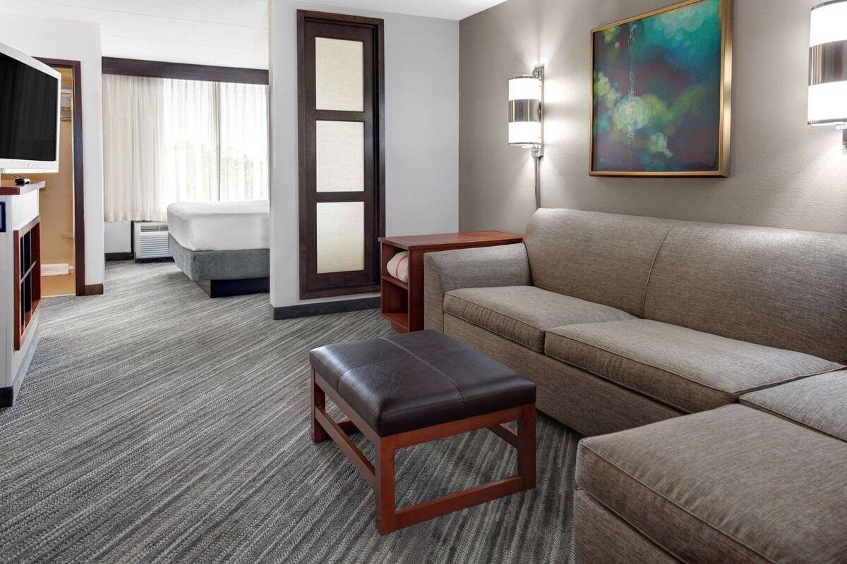 A hotel room with a sofa, a small table, a TV, a painting, and a door.