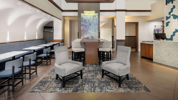 A modern hotel lobby with a central seating area, a reception desk, and a large window providing natural light. - Hyatt Place Busch Gardens (Tampa)