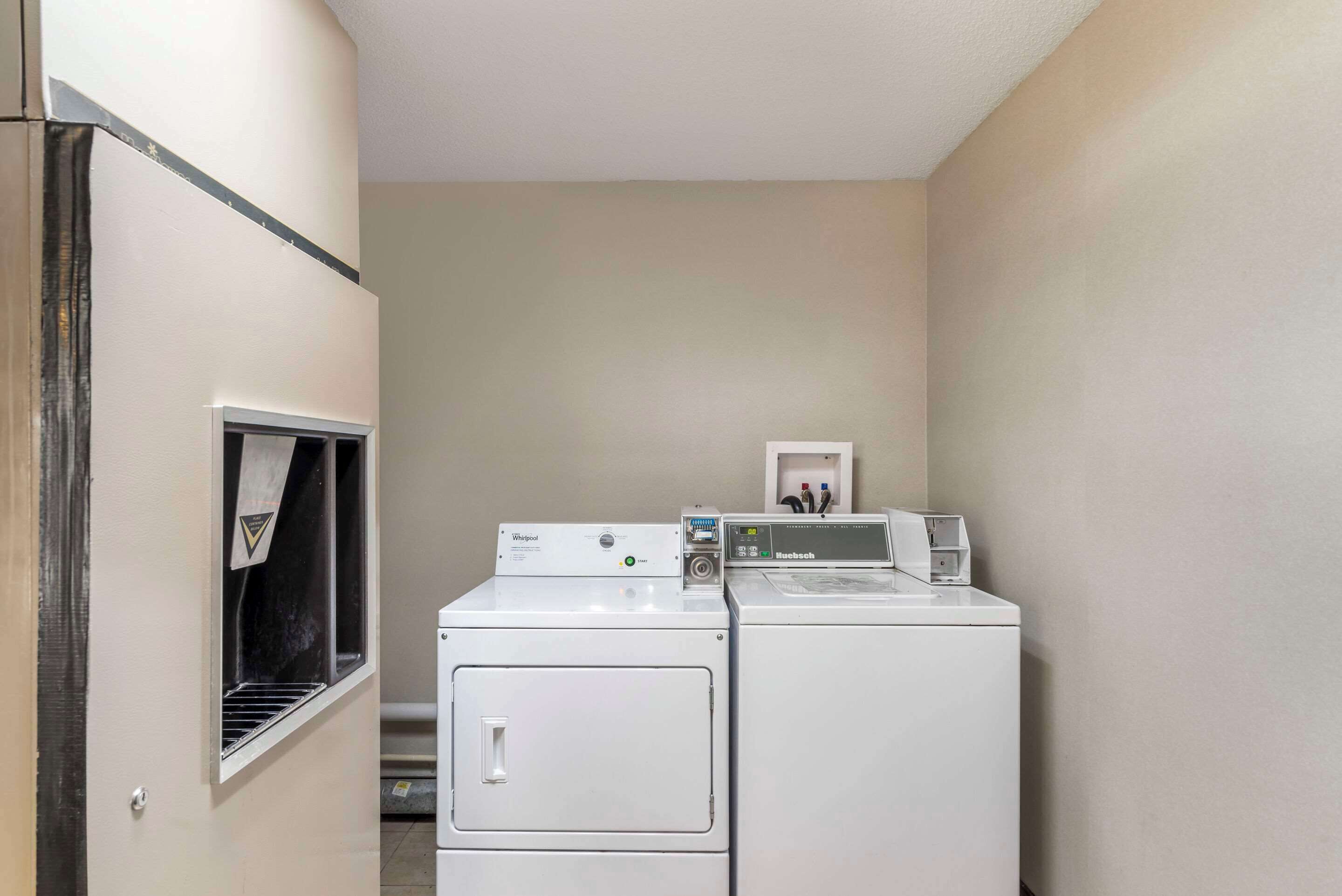 Une buanderie équipée de deux machines à laver et deux sèche-linge superposés, une petite fenêtre avec une serviette qui y est accrochée, et un tableau encadré au mur.