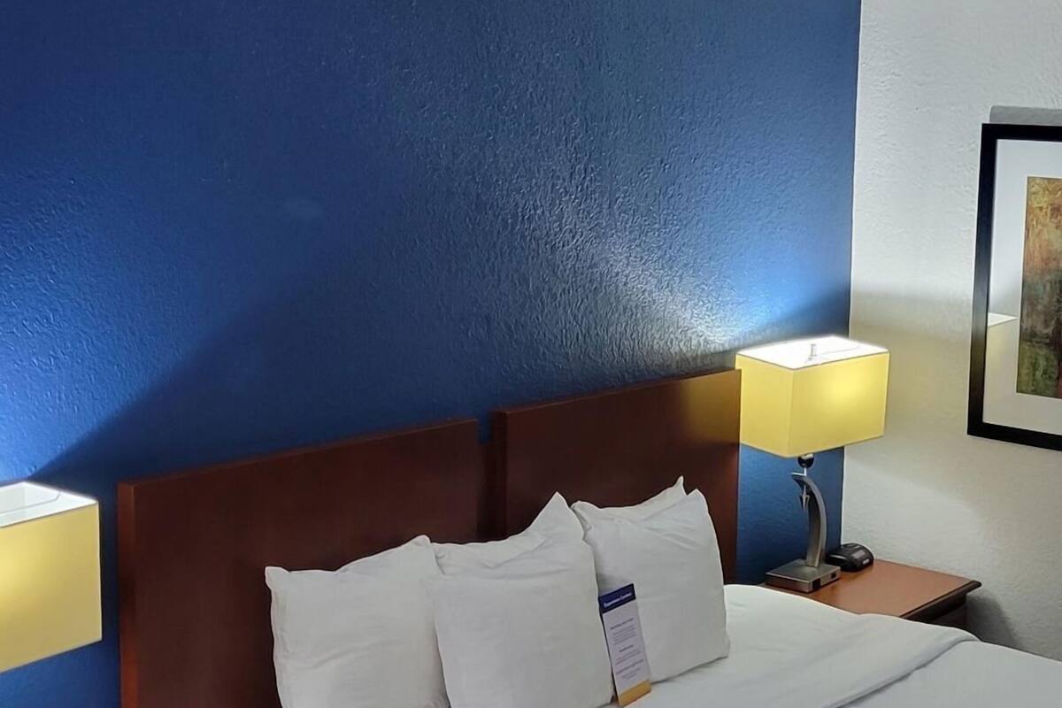 A hotel room with a bed, two bedside tables, a nightstand, a lamp, and a framed picture on the wall.