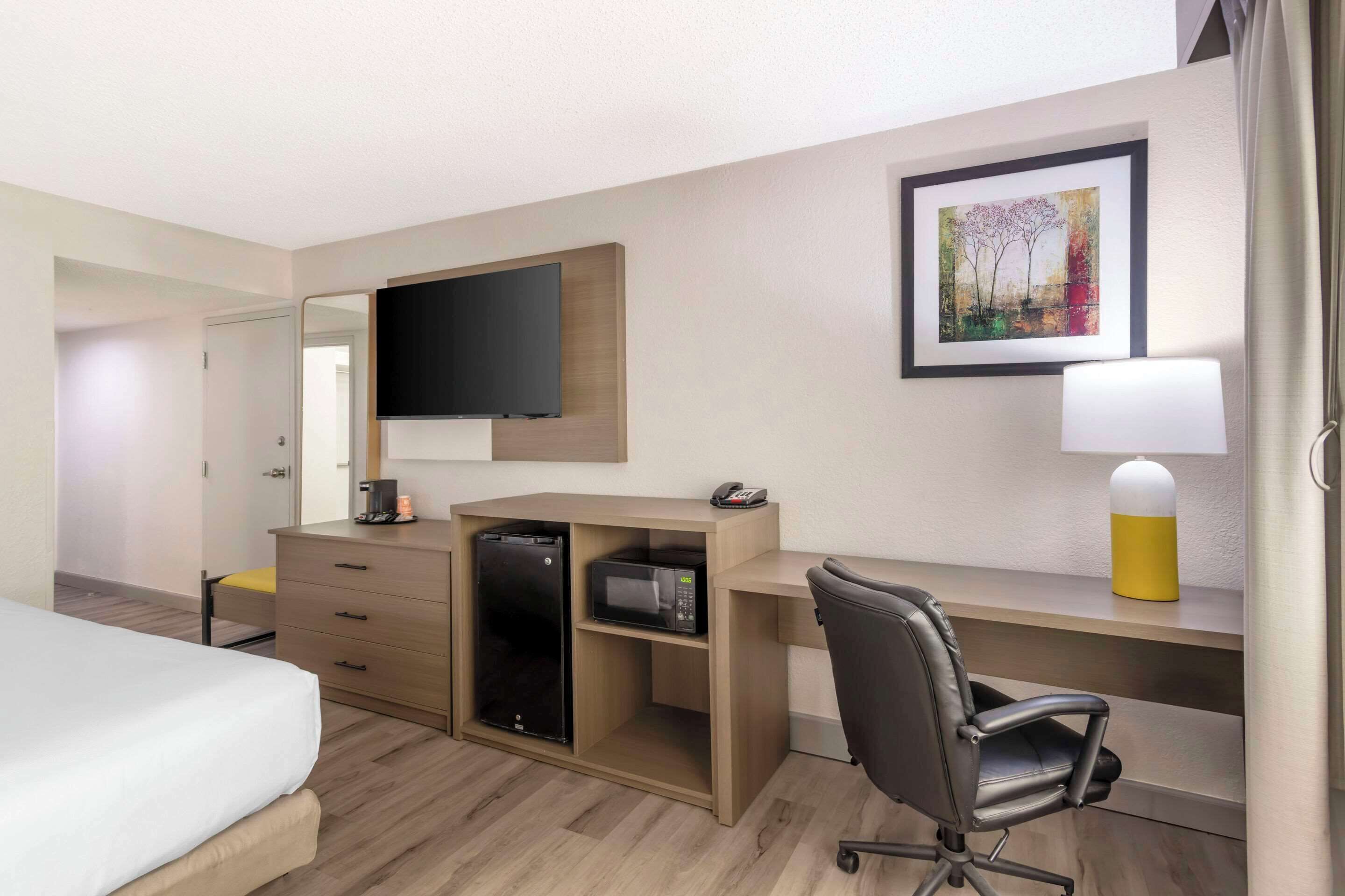 A hotel room with a bed, a desk with a computer, a microwave, and a television.