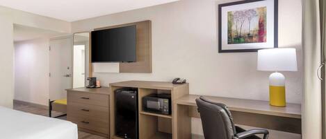 A hotel room with a bed, a desk with a computer, a microwave, and a television.
