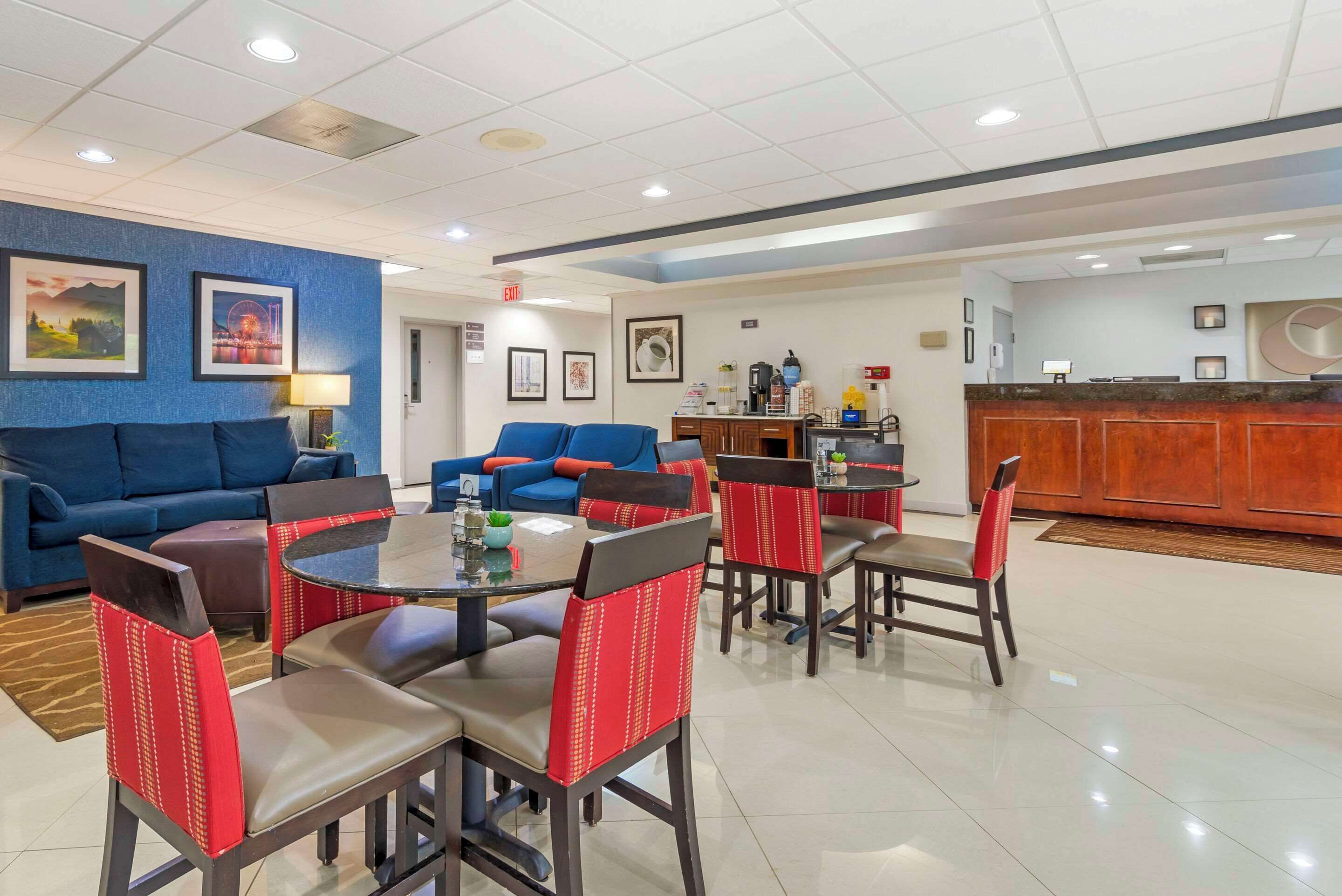 A hotel lobby with a blue wall, a reception desk, a seating area with red and black chairs, and a coffee station.