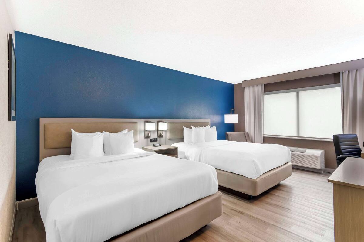 A hotel room with two beds, a desk, a chair, and a window with curtains.