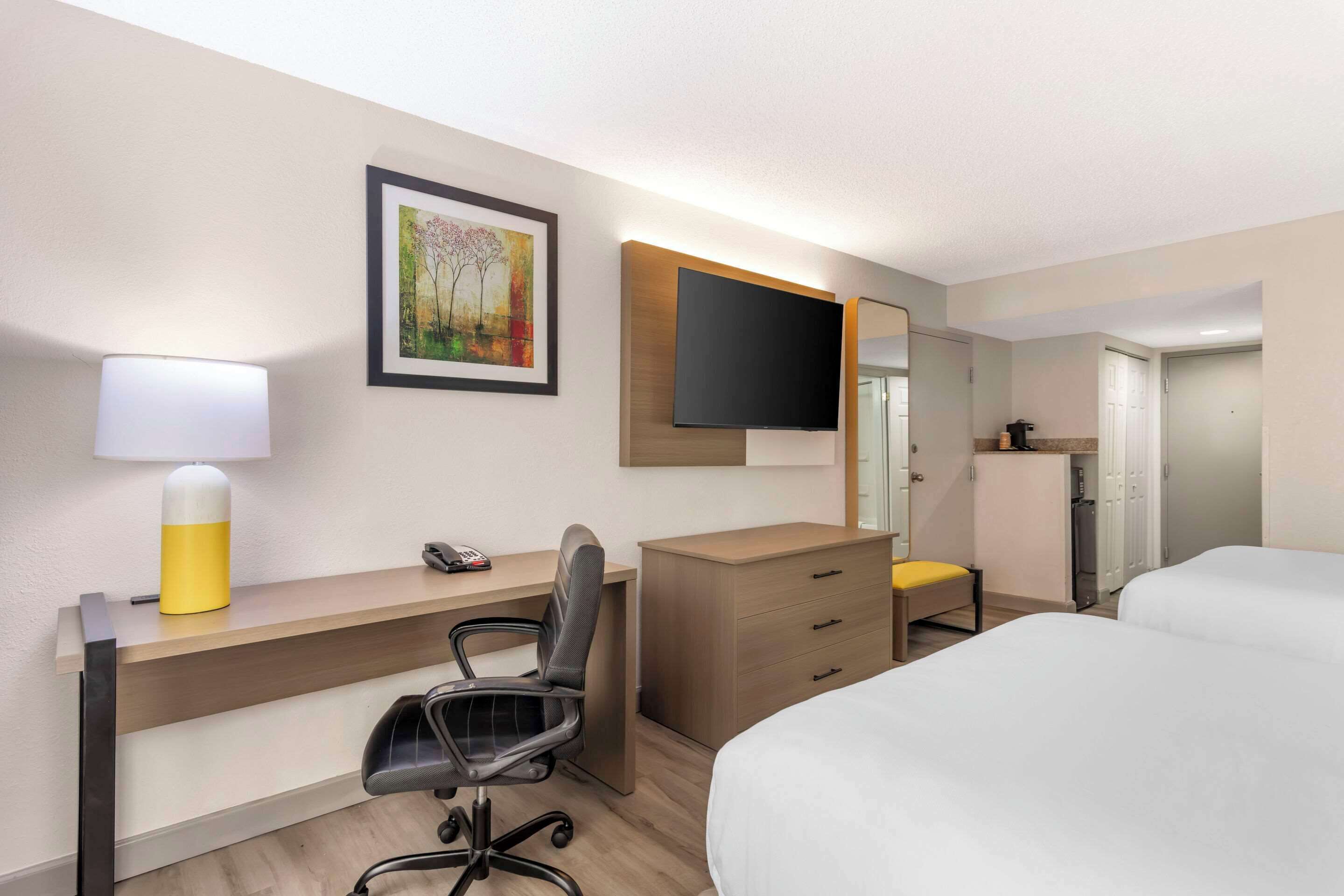 A hotel room with a bed, desk, chair, and a TV mounted on the wall.