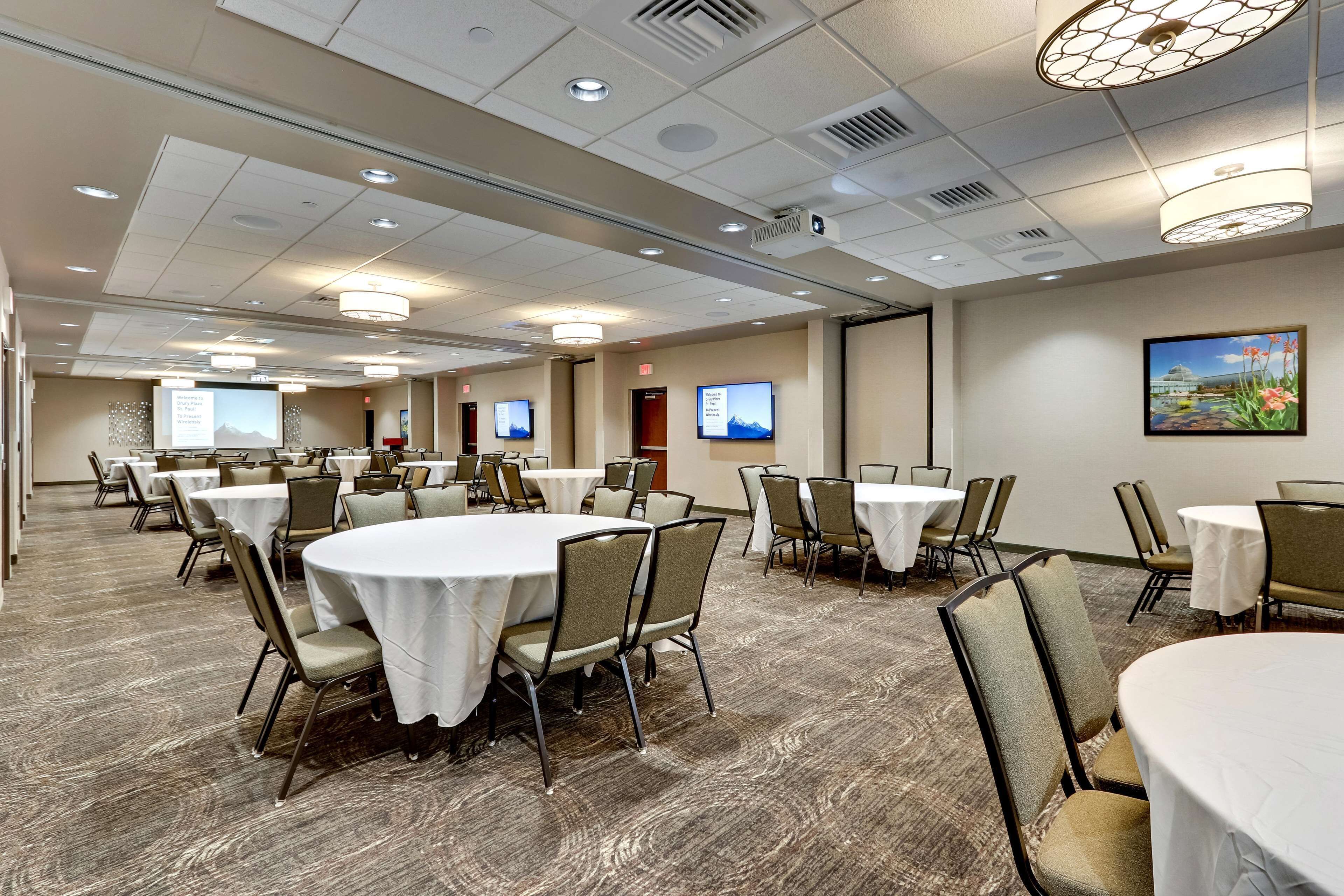 A conference room with round tables and chairs, equipped with ceiling lights and projectors.