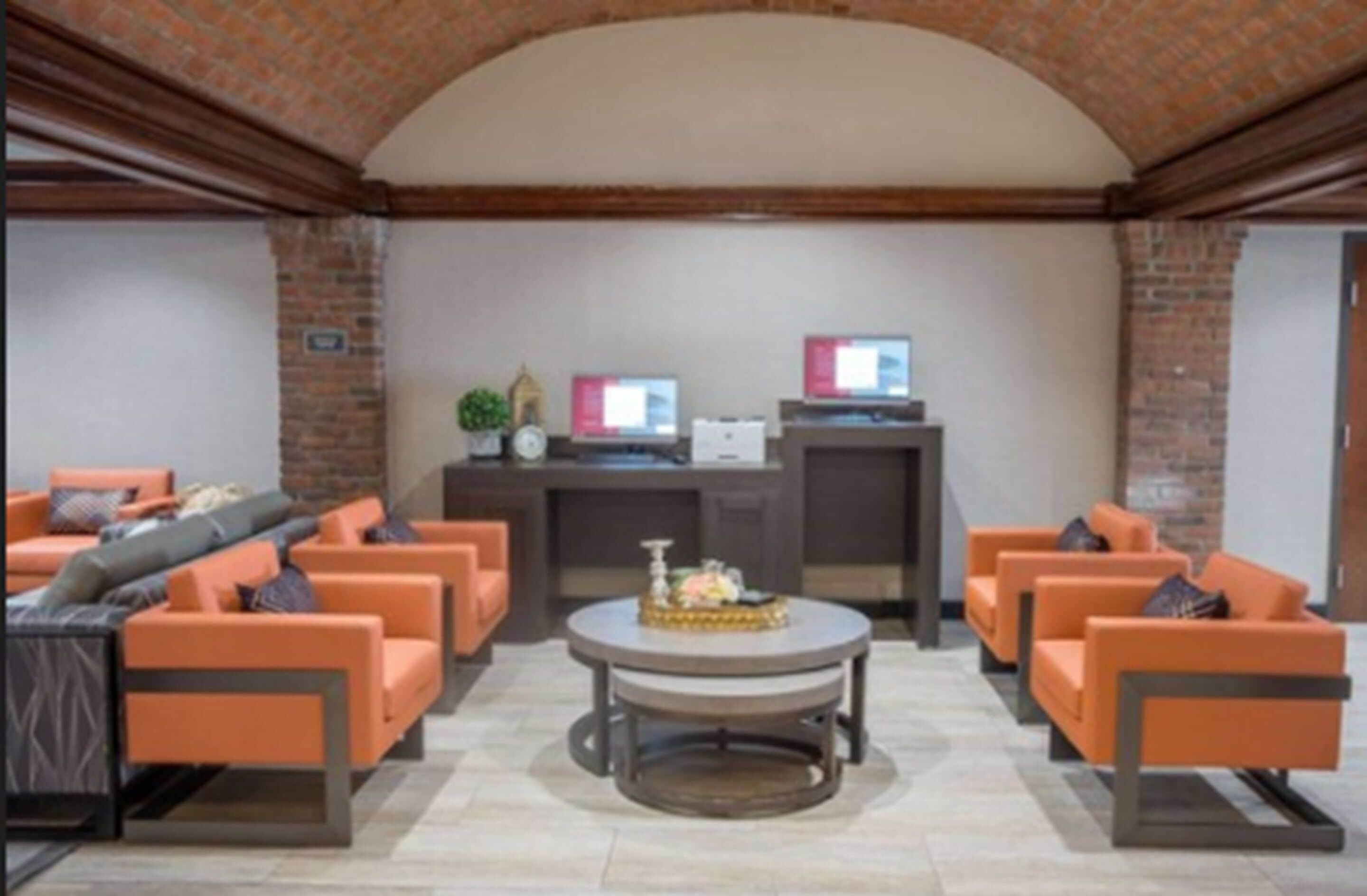 Um hall com sofás laranja, uma mesa de centro redonda e uma parede de tijolos.