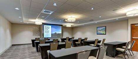 A conference room with a large screen, multiple tables, and chairs arranged for a meeting.