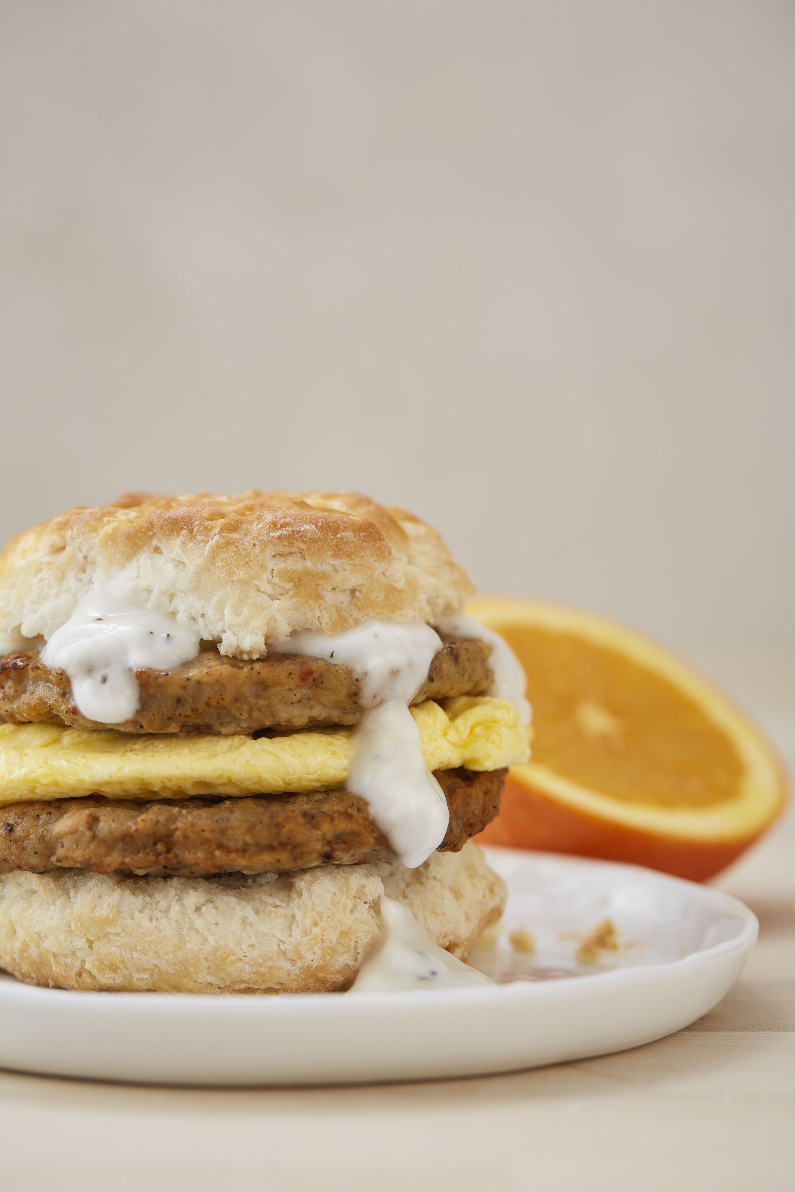 Un sándwich de desayuno sobre un plato, con una rodaja de naranja al fondo.