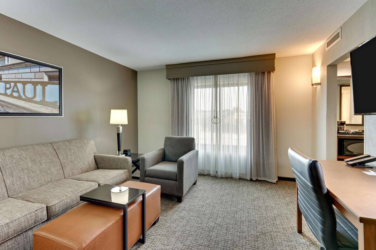 A hotel room with a sofa, armchair, coffee table, and a dining table.
