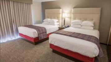 A hotel room with two beds, each with a headboard, a bedside table, and a lamp.