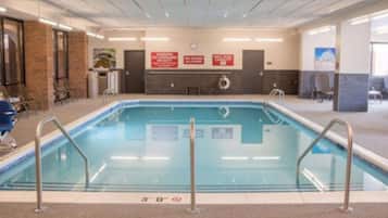 Ein Hallenbad mit deutlicher Sicherheitsschilderung, einem Rettungsschwimmerstuhl und einem Poolbereich mit Stühlen und einer Theke.