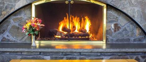A stone fireplace with a fire, a vase of flowers, and a table with a floral tablecloth.