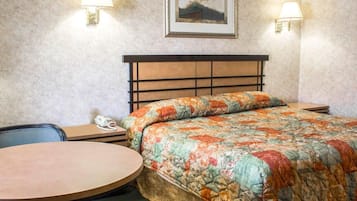 A hotel room with a bed, a round table, two bedside lamps, a framed picture on the wall, and a telephone on the nightstand.