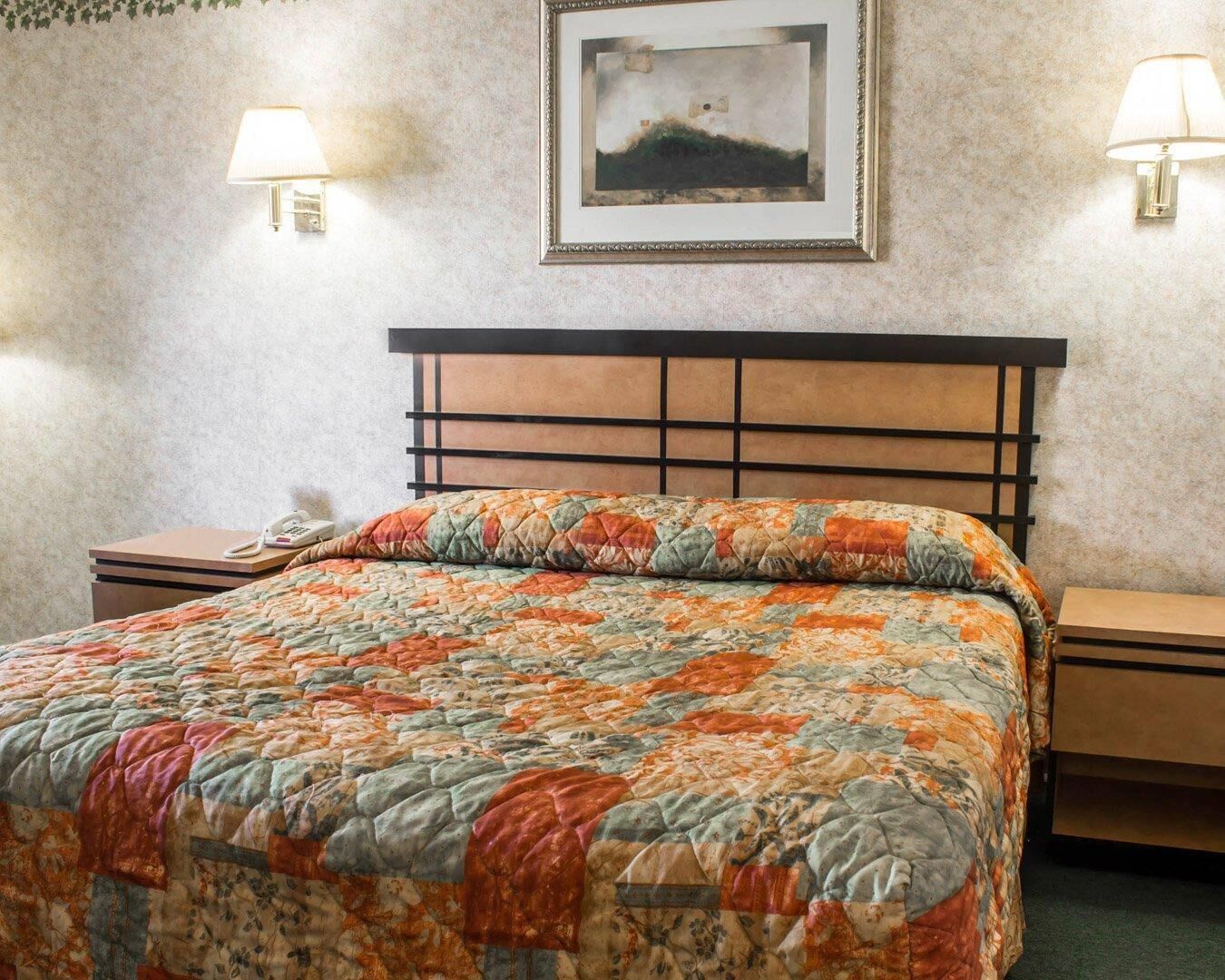 Een bed met een sprei, een nachtkastje met een lamp, en een ingelijste foto aan de muur.