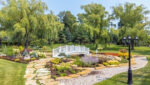 Un jardin aménagé avec un pont blanc, un sentier de pierres et différentes espèces de plantes.