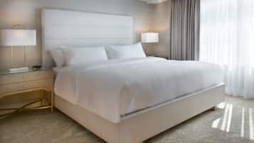 A modern hotel room with a large bed, two bedside tables with lamps, and a view of the outdoors through sheer curtains.