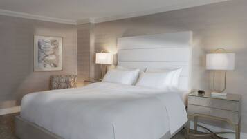 A neatly arranged hotel room with a large bed, two bedside tables with lamps, a framed artwork on the wall, and a patterned chair.