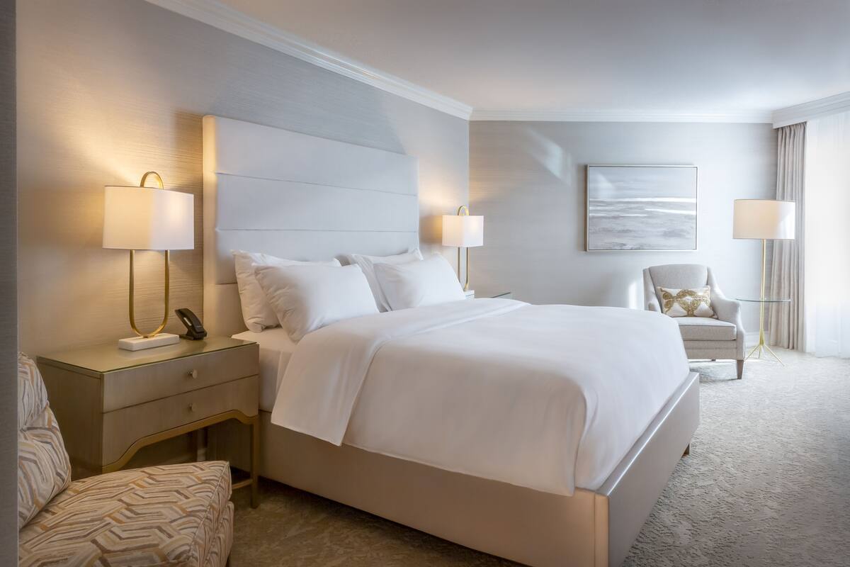 Une chambre d’hôtel avec un grand lit, deux tables de chevet avec des lampes, une chaise et un tableau encadré au mur.