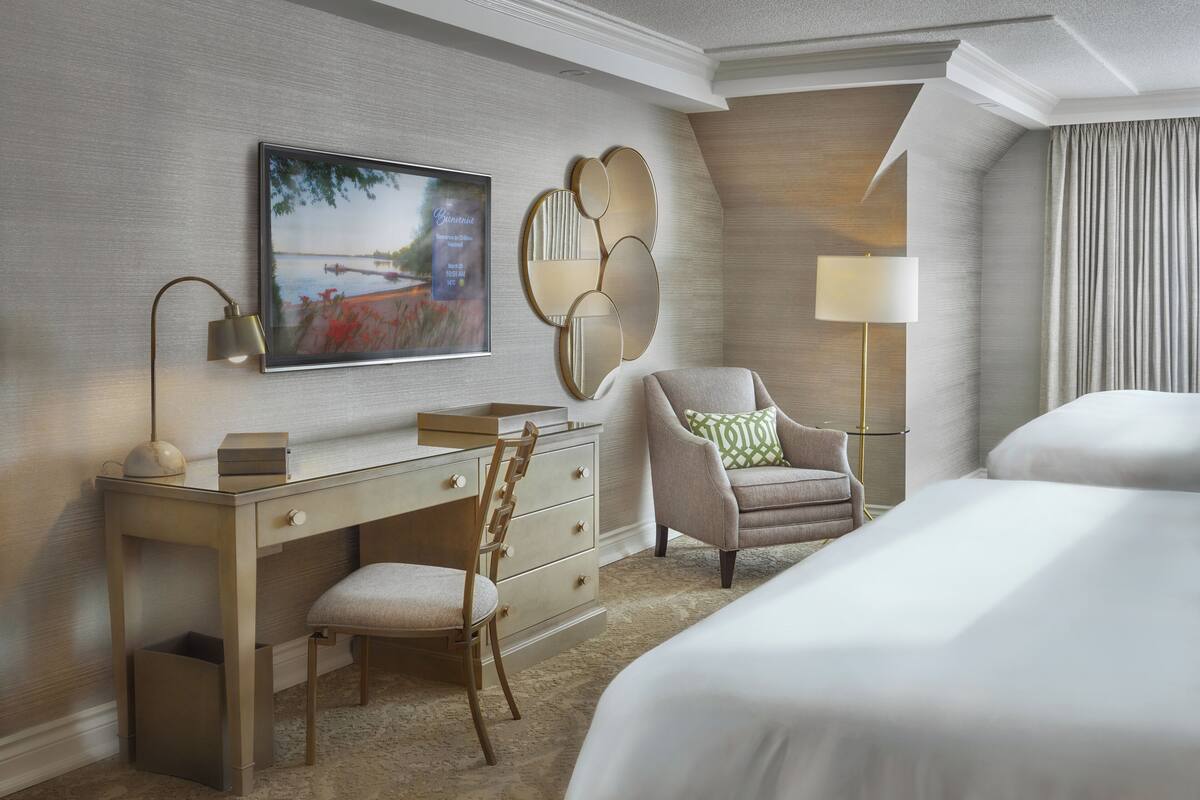 Une chambre d’hôtel comprenant un lit, un bureau avec une chaise, une télévision, une lampe et un miroir décoratif.