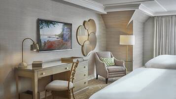 A hotel room with a bed, a desk with a chair, a television, a lamp, and a decorative mirror.