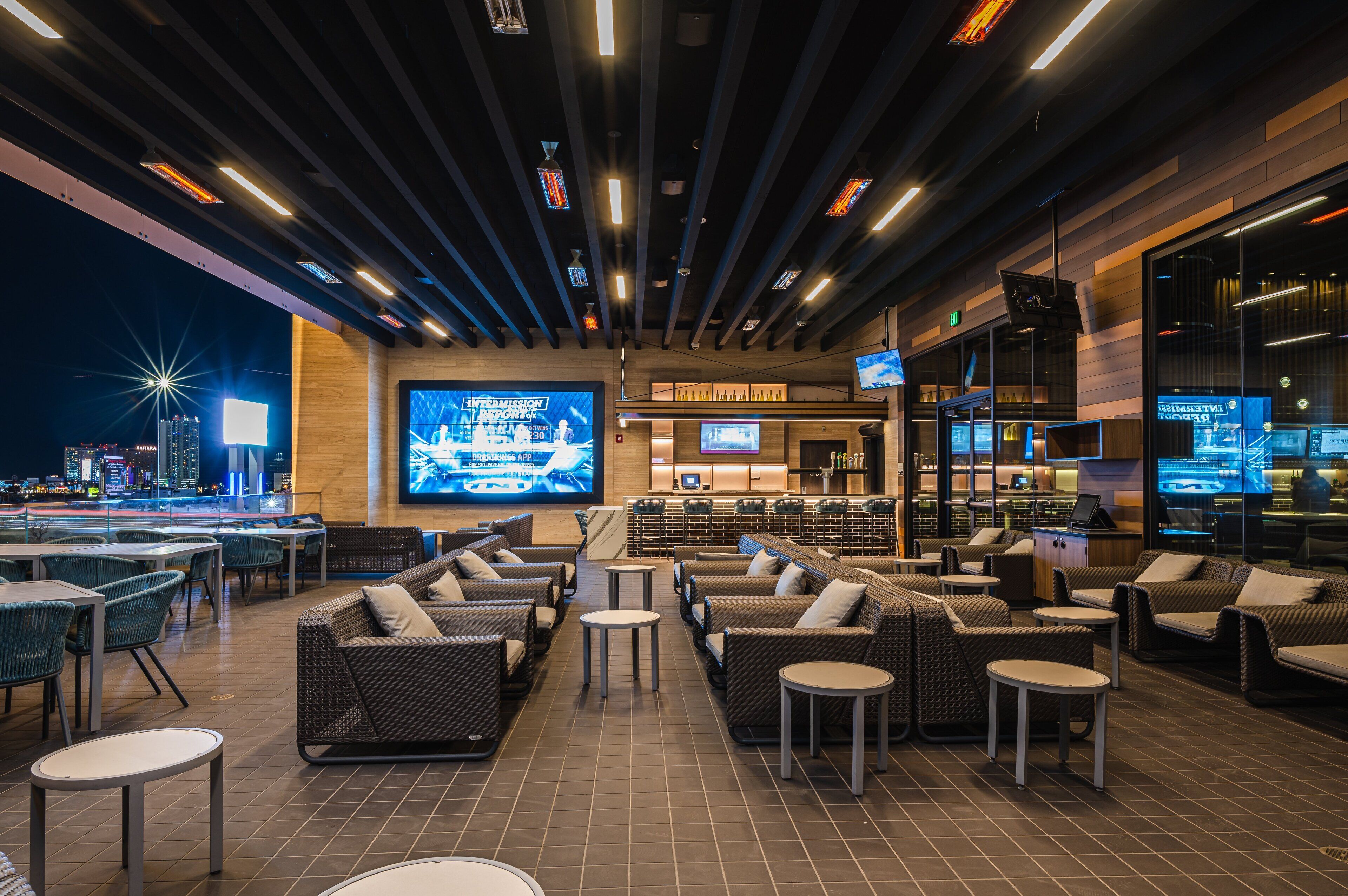 A modern lounge area with comfortable seating, a bar, and large screens displaying content.
