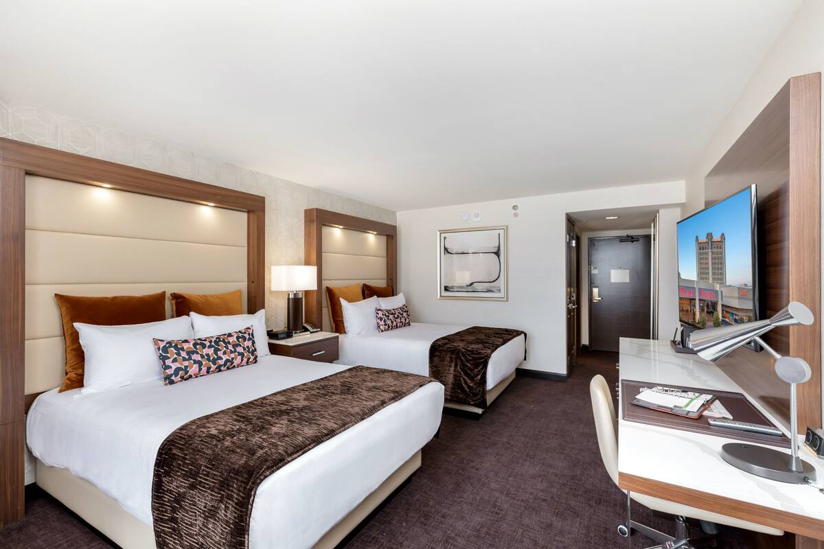 A hotel room with two beds, a desk, a chair, a TV, and a door leading to a bathroom.