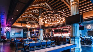 A spacious restaurant with high wooden ceilings, large chandeliers, and a long communal table.
