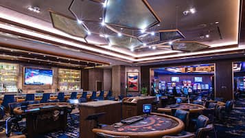 Kasino, jossa on useita blackjack-pöytiä, kolikkopelejä ja suuri televisioruutu, jolta näkyy urheilutapahtuma.