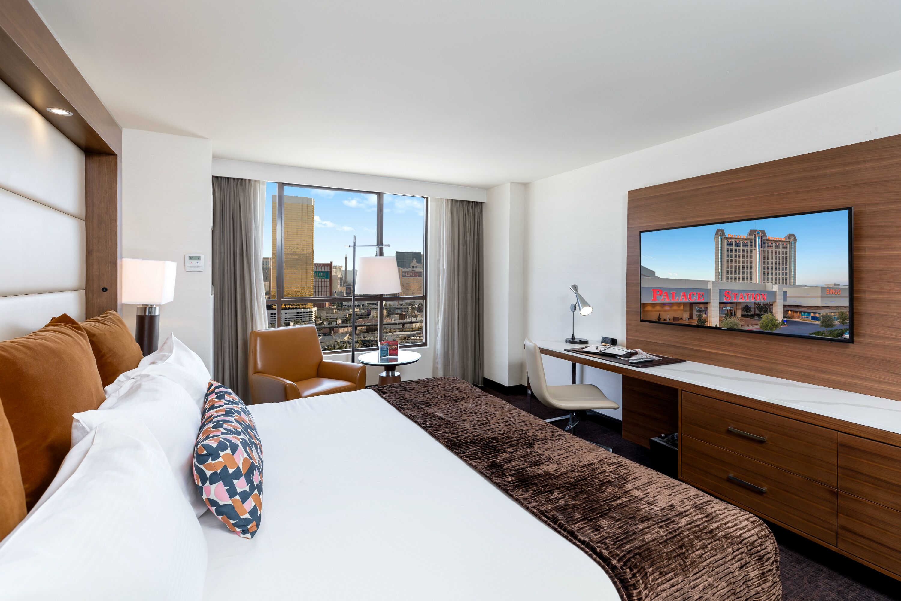 Habitación de hotel con una cama grande, un escritorio, una silla, un televisor y vista a la ciudad.