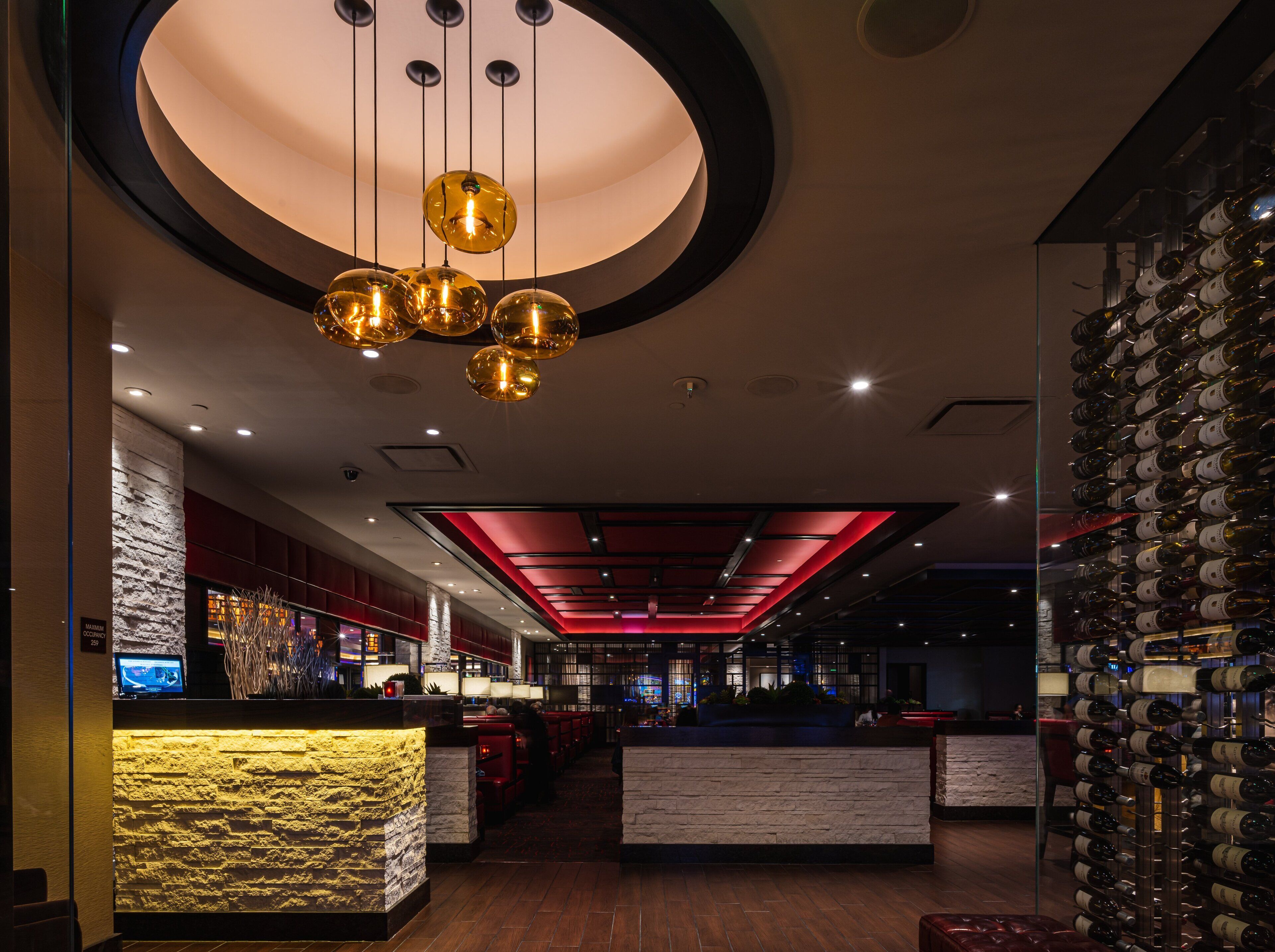 A modern hotel lobby with a stone reception desk, a wine rack, and a ceiling with hanging spherical lights.