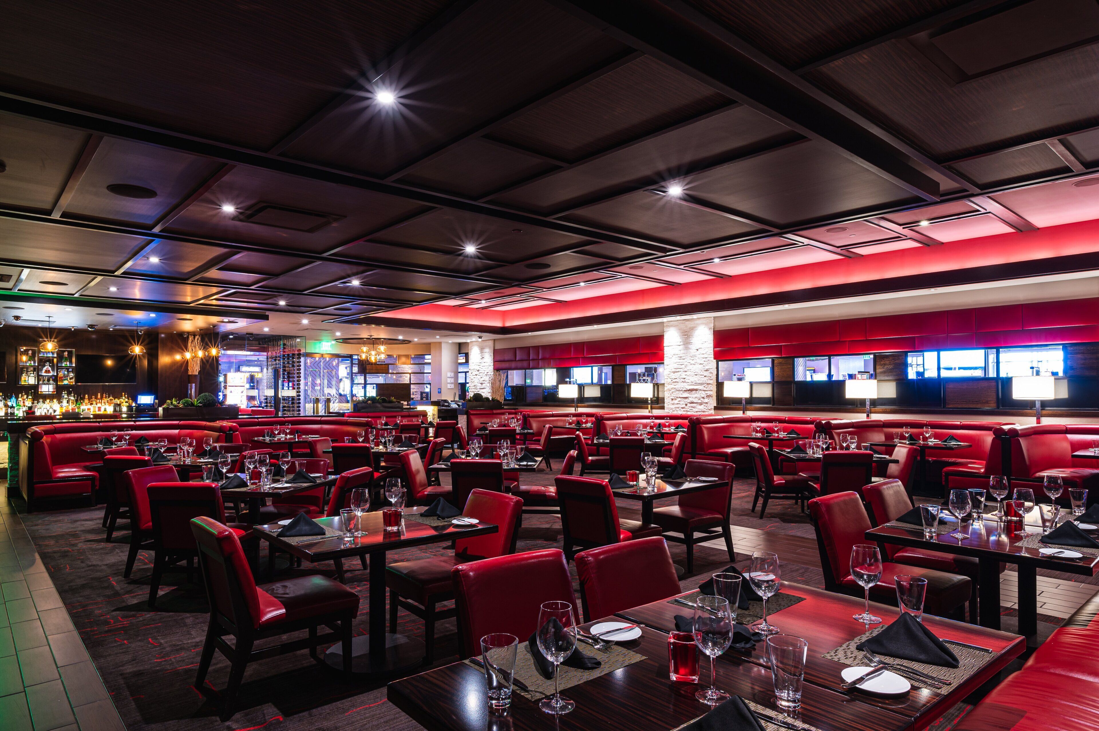 Un restaurante con mesas y cabinas rojas, una zona de bar y una pared decorativa de piedra.