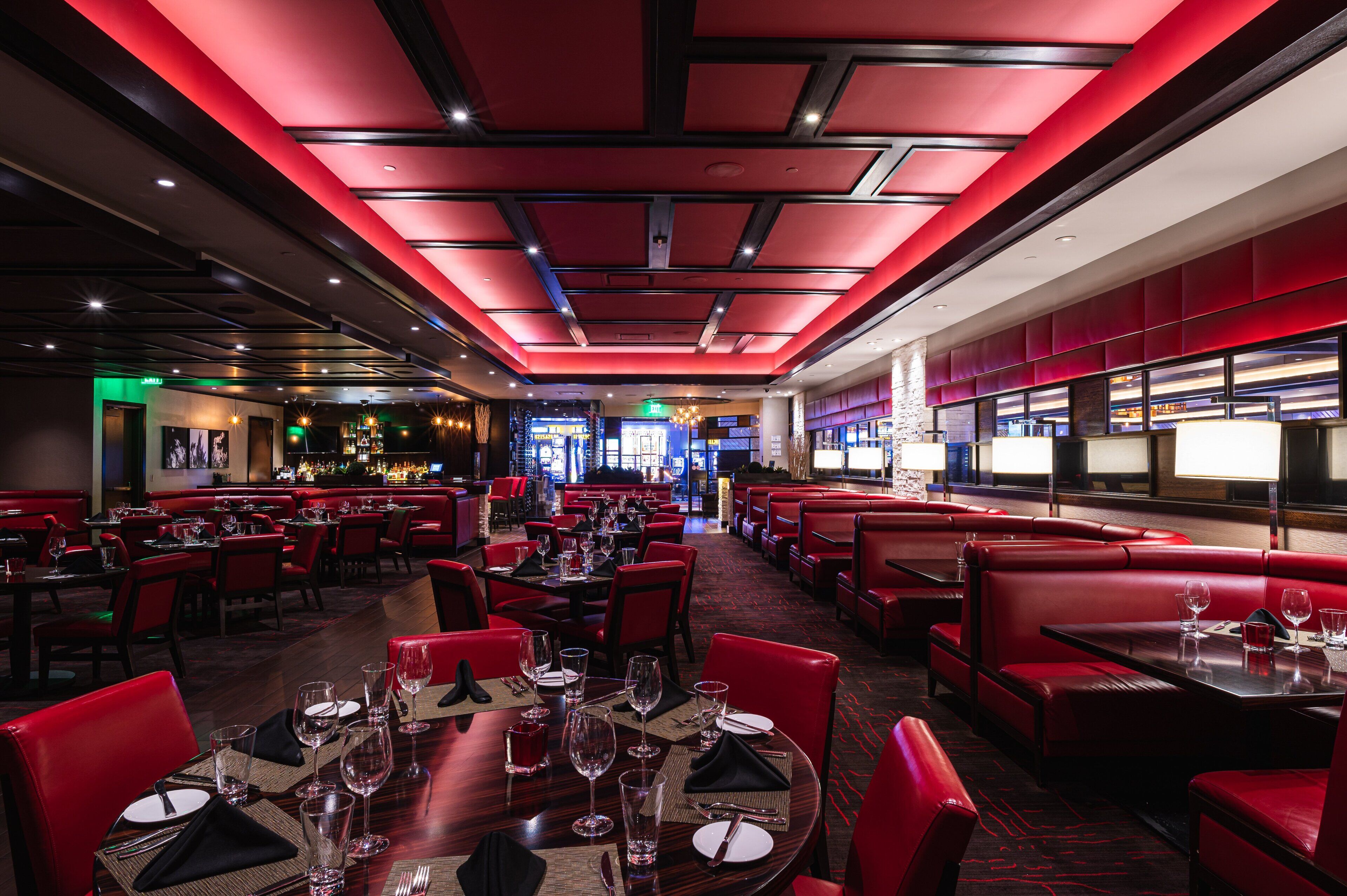Ein Restaurant mit roten Sitzecken und Tischen, eine Bar im Hintergrund und eine rote Decke.