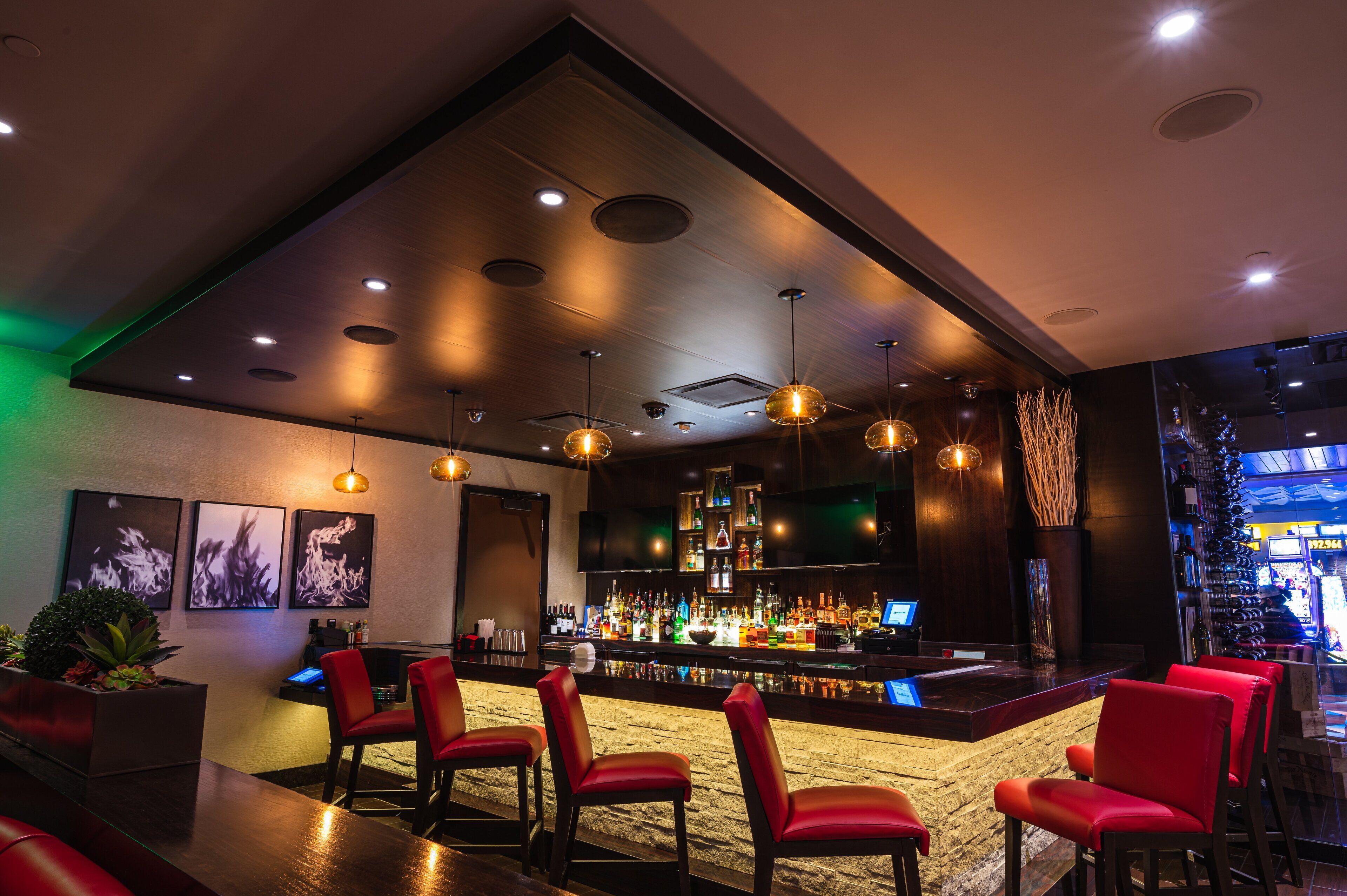 A bar area with red chairs, a bar counter, and a variety of bottles.