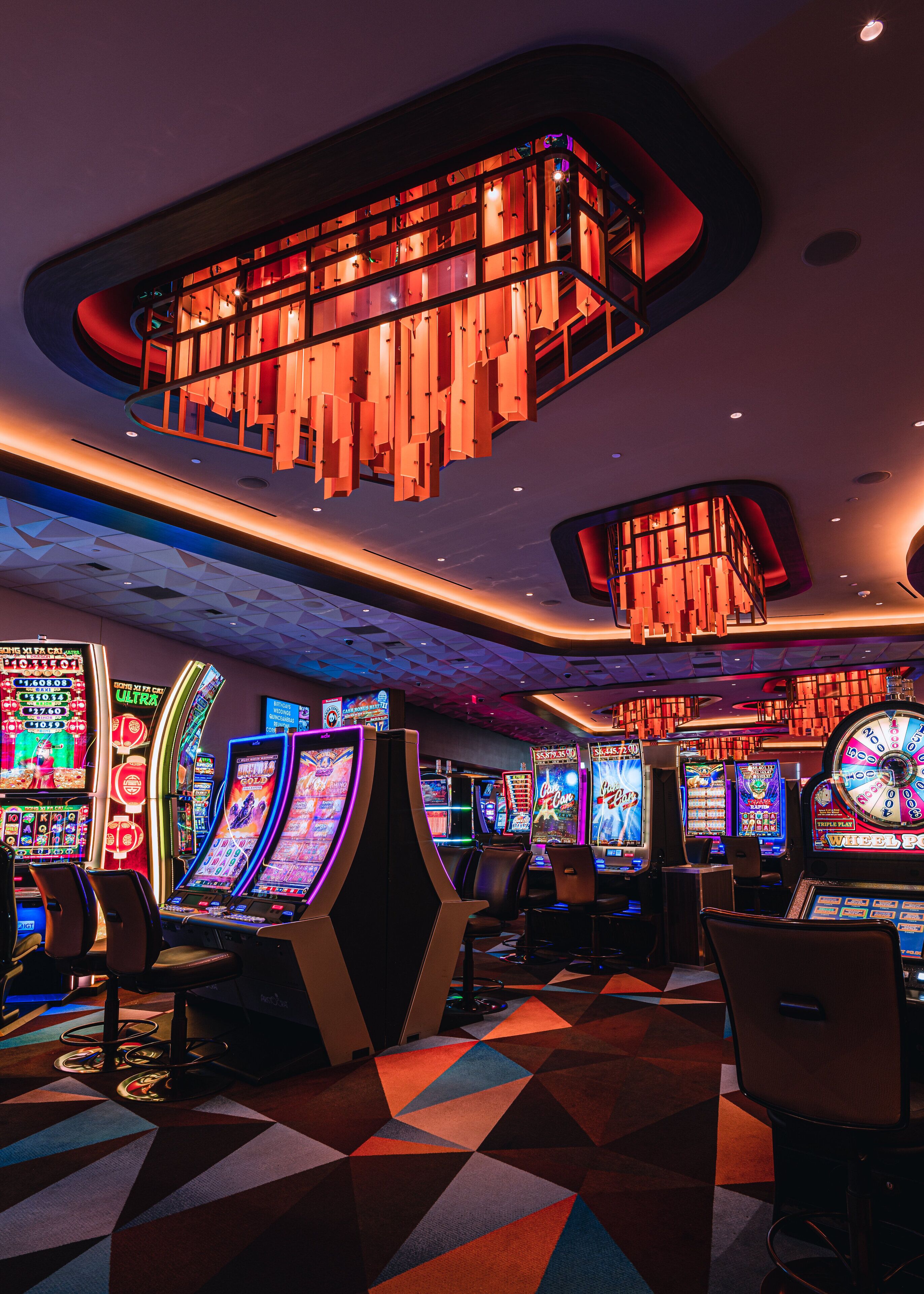 A casino interior with slot machines, a geometric patterned floor, and modern lighting fixtures.