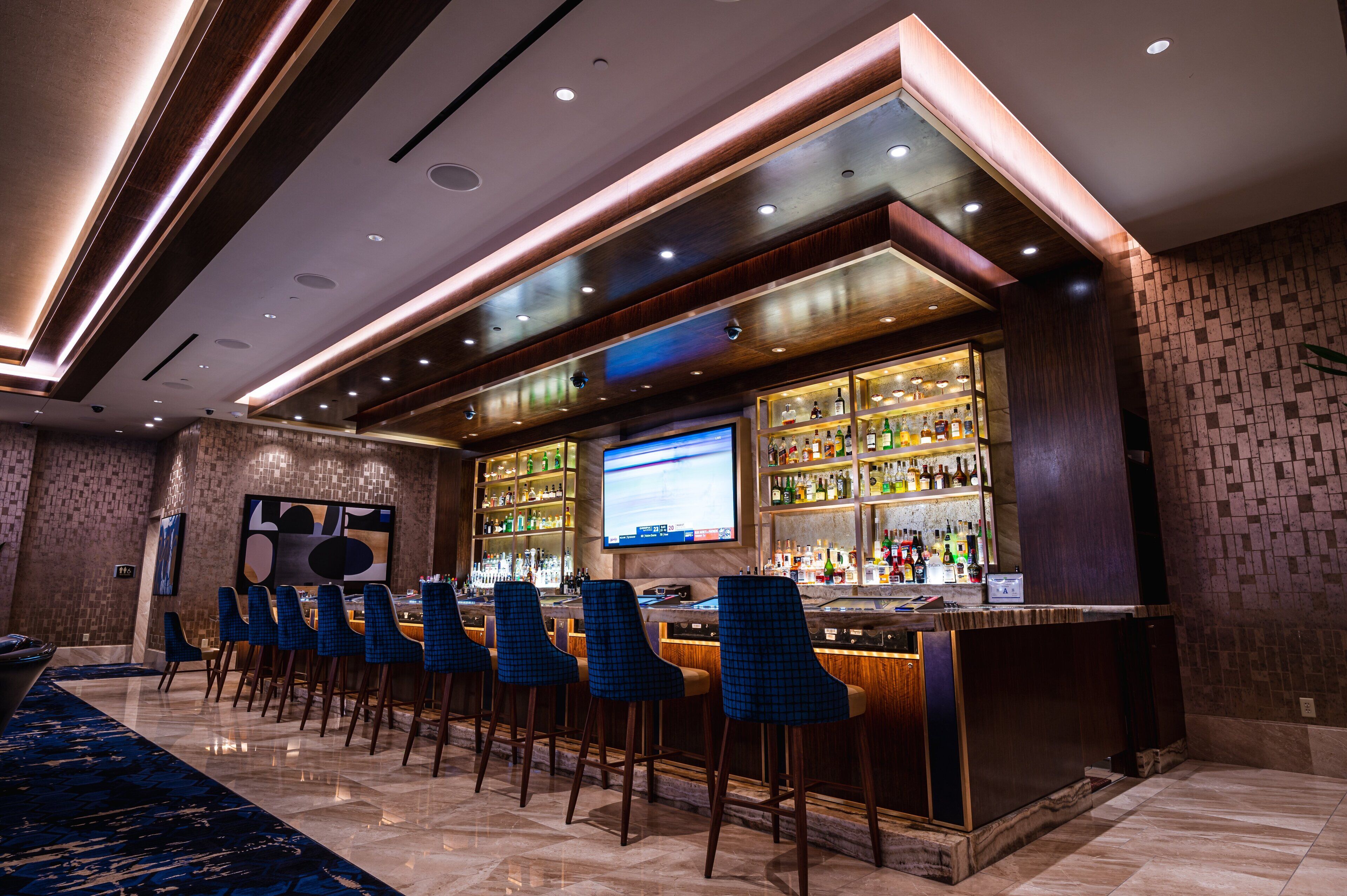 A bar area with a long counter, multiple bar stools, and a television screen.