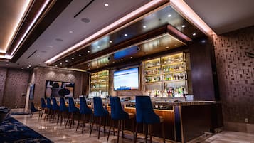 A bar area with a long counter, multiple bar stools, and a television screen.