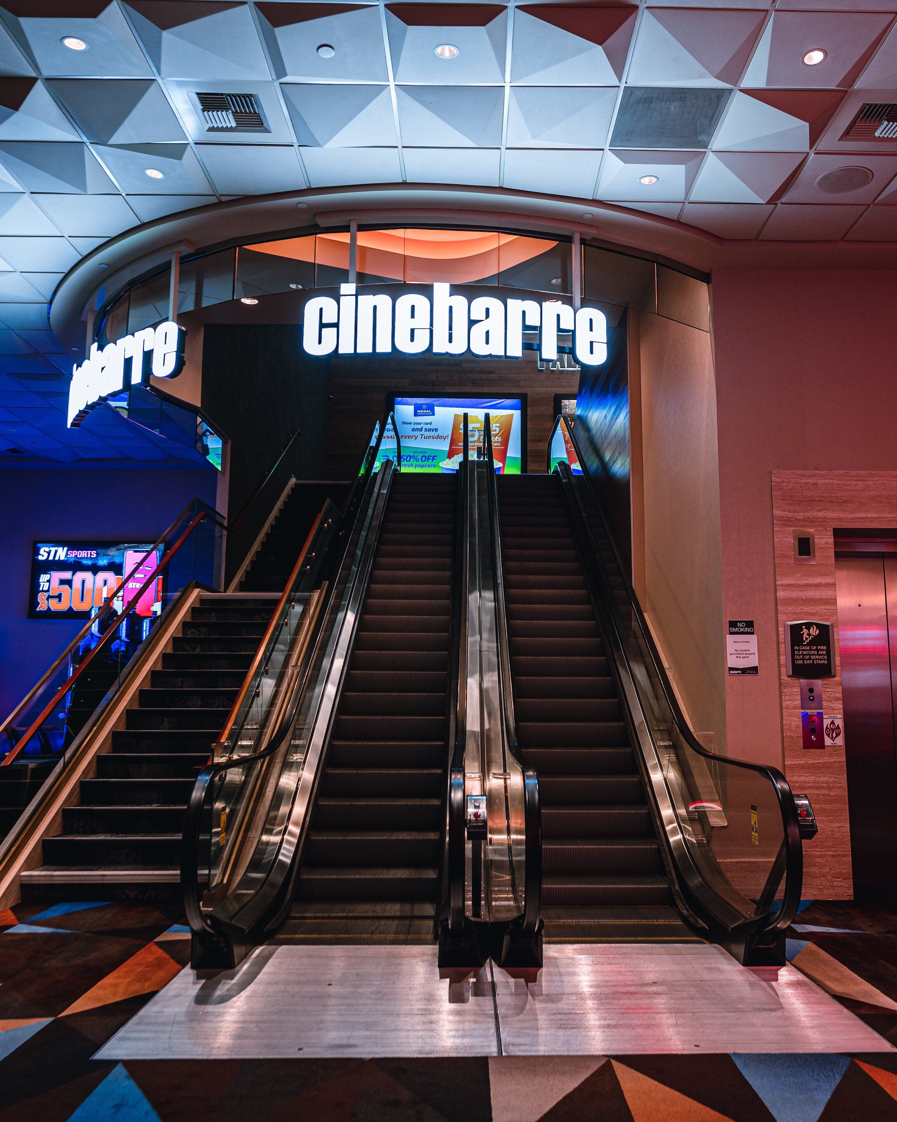 Een bioscoop met een 'cinobarre' bord, roltrappen en een reclamescherm waarop 50% korting wordt aangeboden.