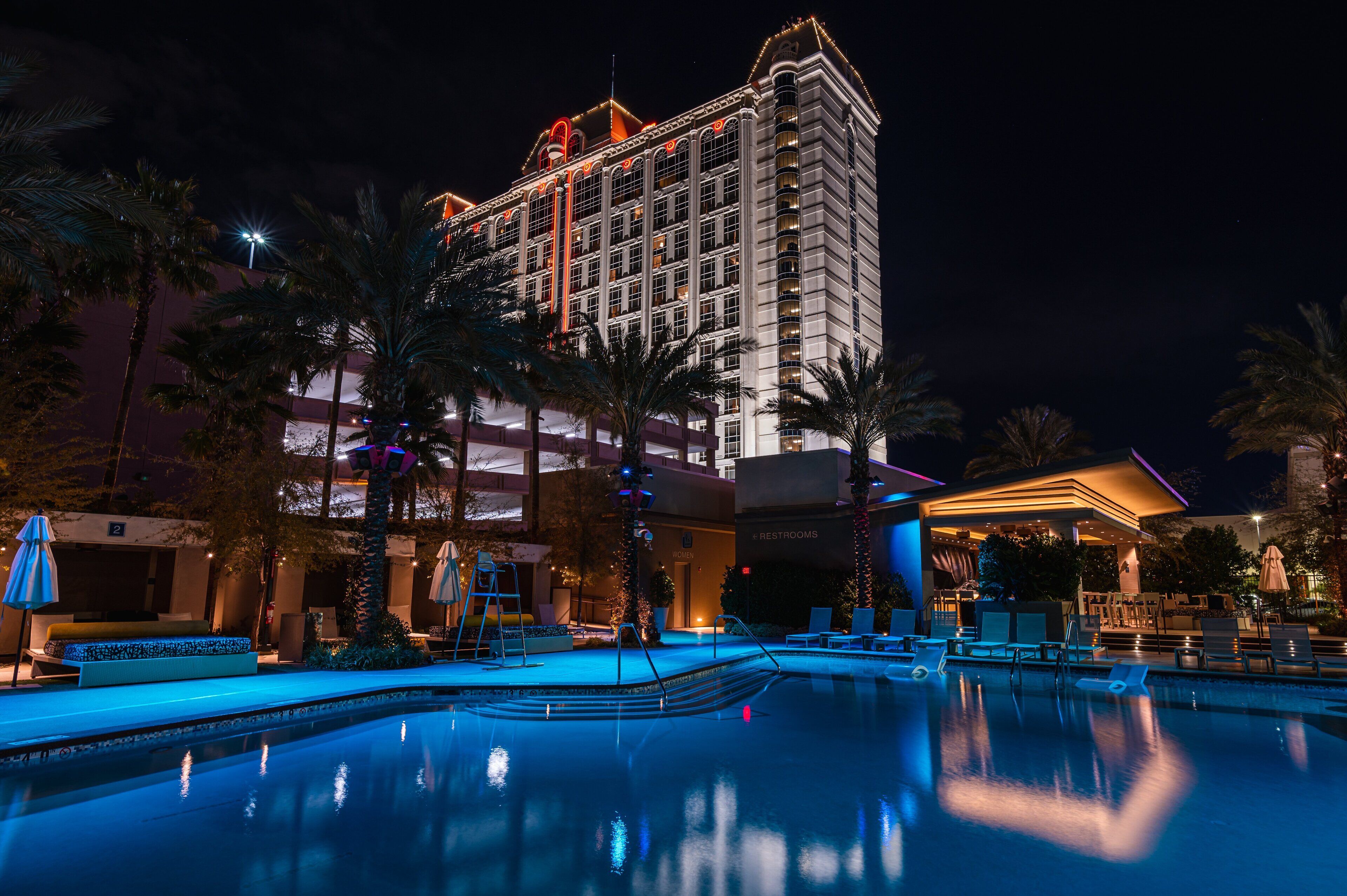 Un hotel con piscina, palmeras y una fachada bien iluminada durante la noche.