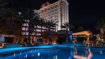 Un hotel con piscina, palmeras y una fachada bien iluminada durante la noche.