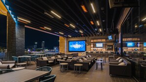 An outdoor bar area with seating, a large screen, and a view of the cityscape.