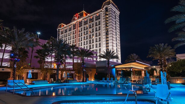 A hotel with a large pool area, palm trees, and a well-lit building facade.