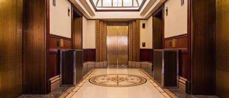 A spacious elevator area with a polished marble floor and wood paneling.