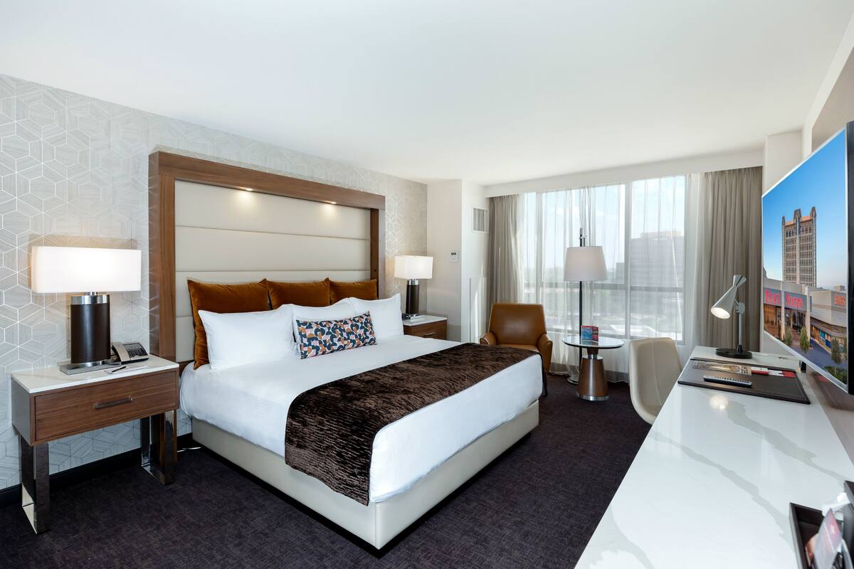 A hotel room with a large bed, bedside tables, a desk, and a television.