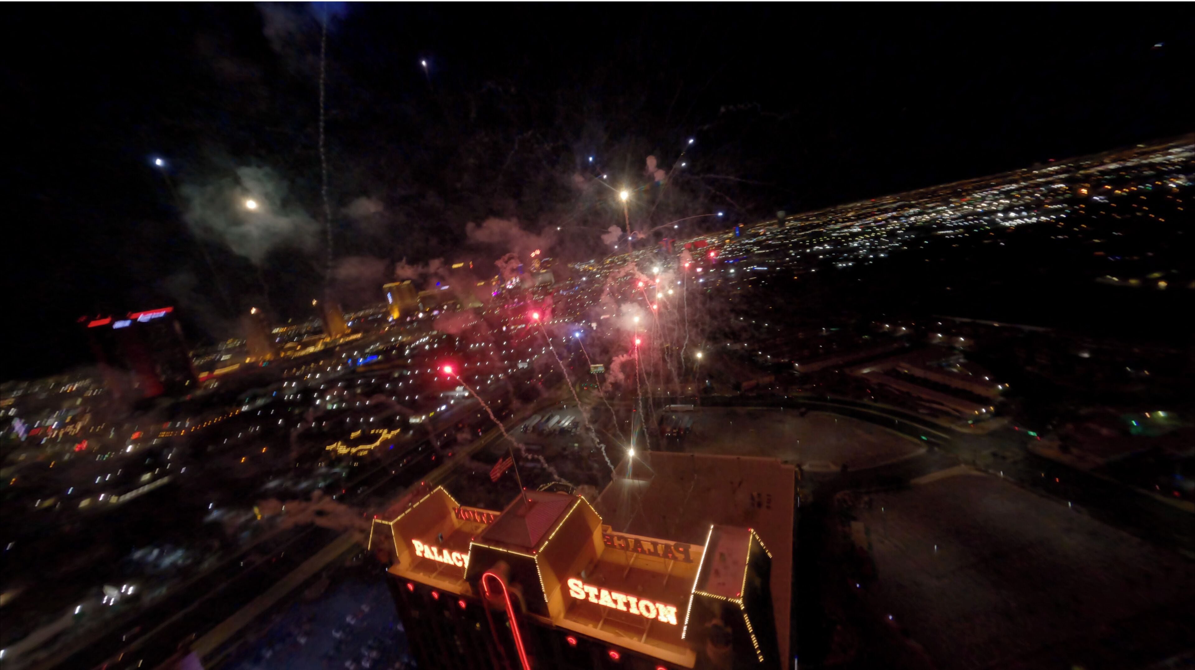 A nighttime aerial view of a city with a prominent building labeled 'PALACE STATION' and fireworks in the sky.