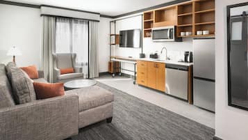 Une chambre d’hôtel moderne équipée d’un canapé, d’un bureau, d’un coin cuisine et d’une télévision.